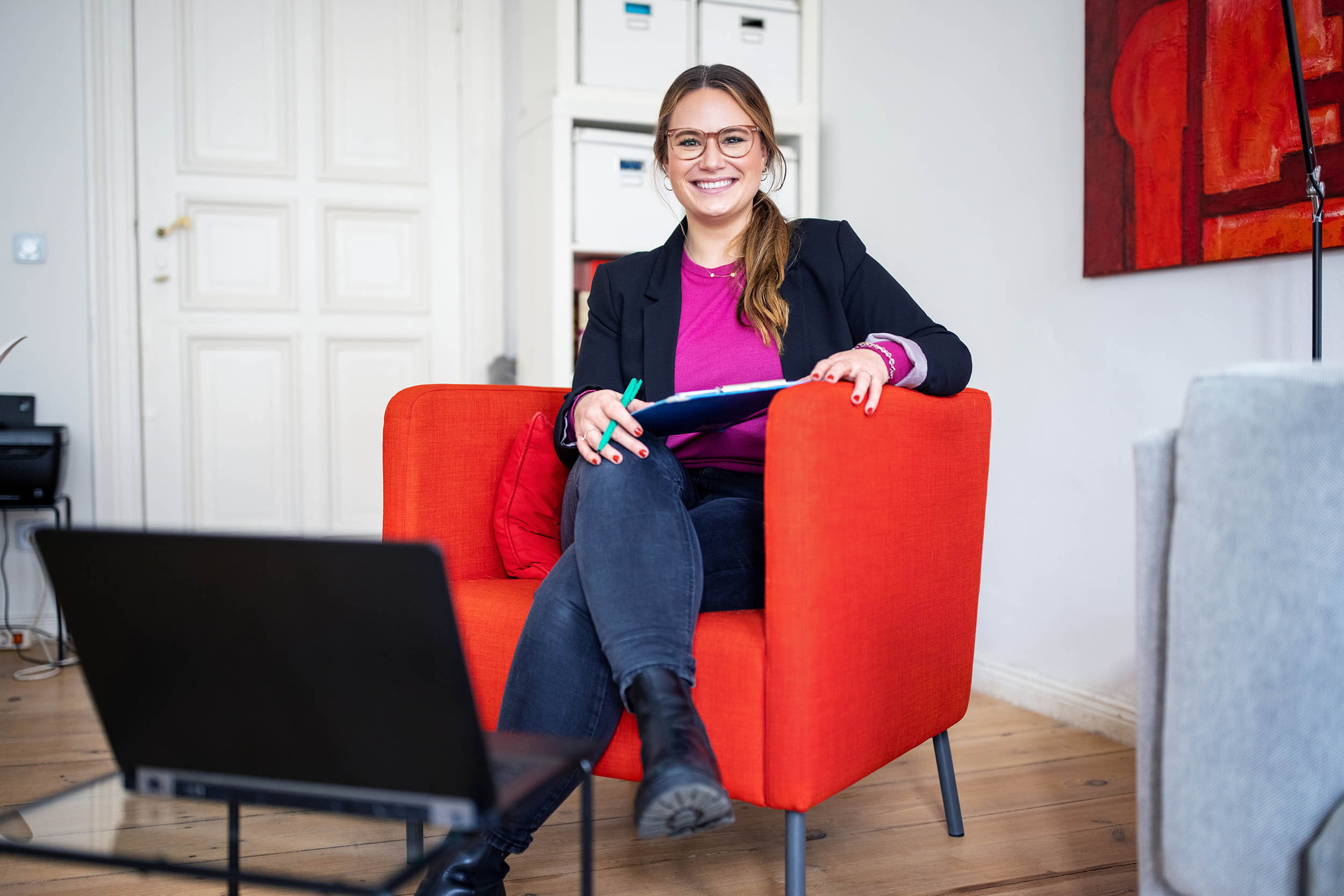 Portrait of a successful female psychologist sitting in arm chair with laptop in front. Happy mental health professional.